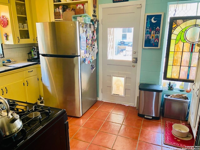 kitchen featuring stainless steel fridge, backsplash, light tile floors, and range