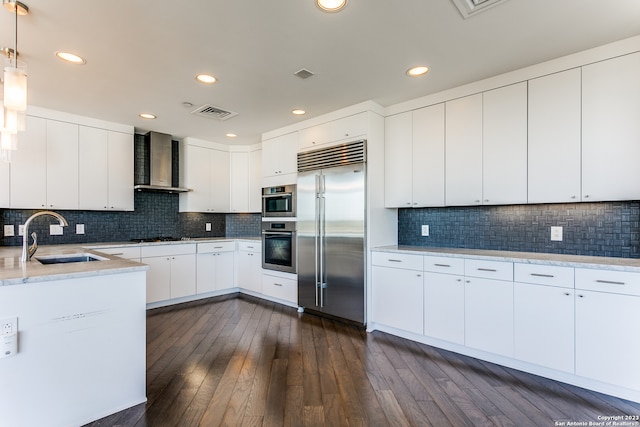 kitchen featuring stainless steel appliances, tasteful backsplash, wall chimney range hood, and white cabinetry