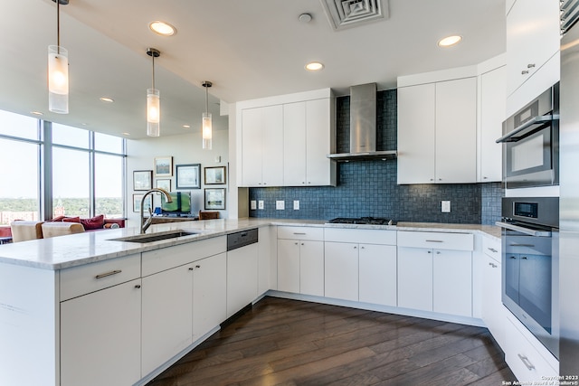 kitchen featuring white cabinetry, wall chimney range hood, hanging light fixtures, and tasteful backsplash