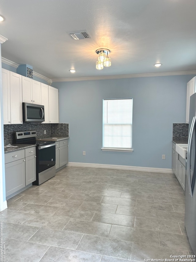 kitchen featuring light tile flooring, white cabinetry, backsplash, ornamental molding, and appliances with stainless steel finishes