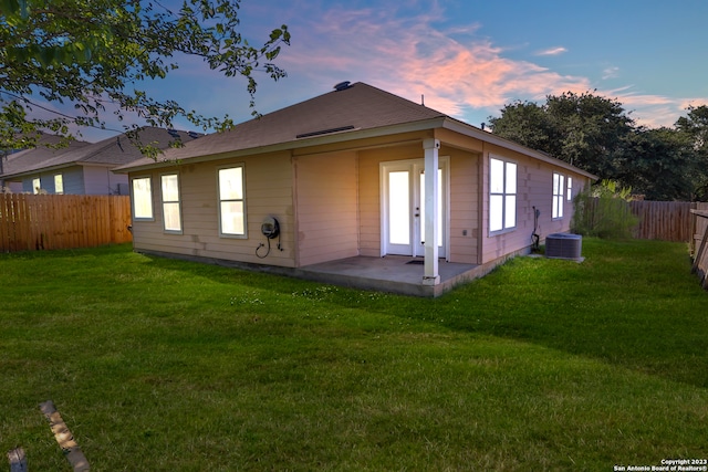 back house at dusk featuring a patio, central air condition unit, and a lawn