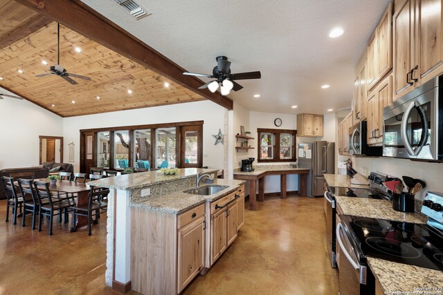 kitchen featuring a kitchen island with sink, ceiling fan, sink, appliances with stainless steel finishes, and light stone countertops