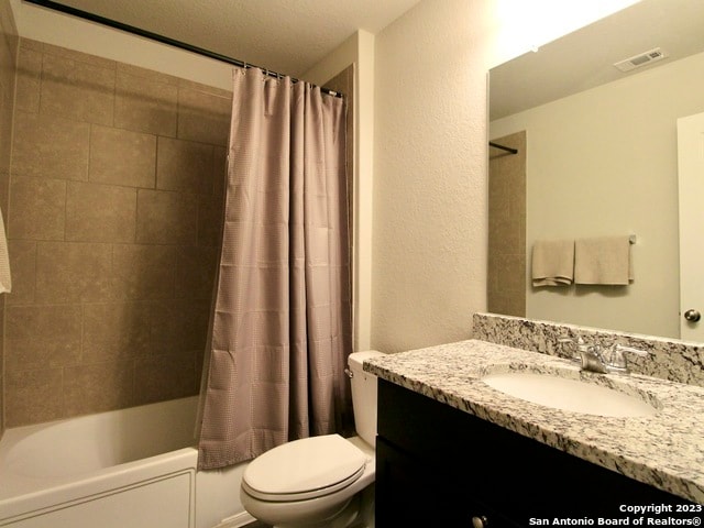 full bathroom featuring a textured ceiling, toilet, vanity, and shower / bath combo with shower curtain