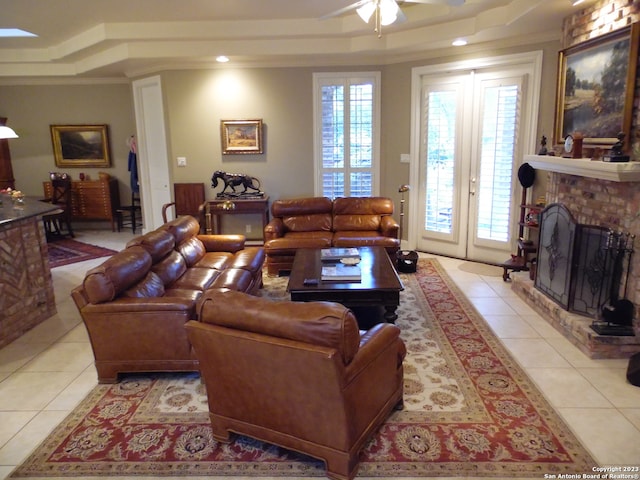 living room with a fireplace, light tile floors, ceiling fan, and a raised ceiling