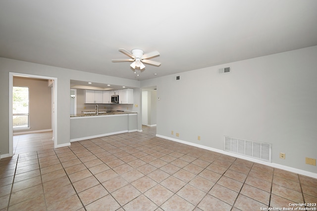 unfurnished living room featuring ceiling fan, sink, and light tile flooring