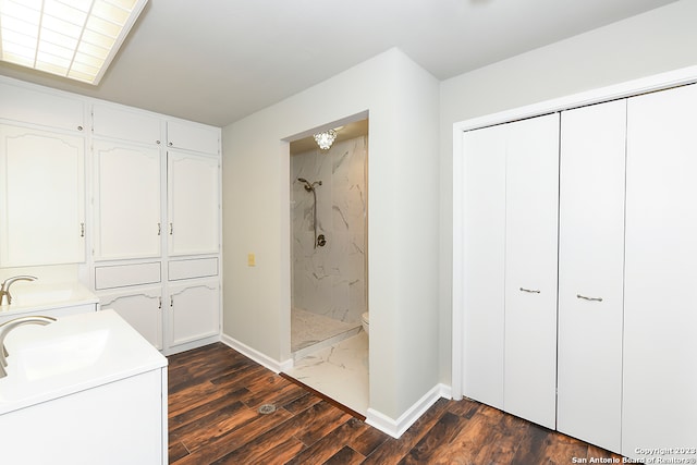 bathroom with toilet, tiled shower, double vanity, and wood-type flooring