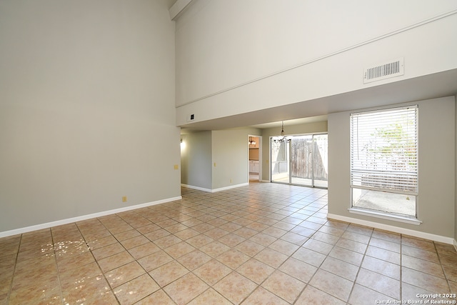 spare room with a chandelier, a high ceiling, and light tile floors