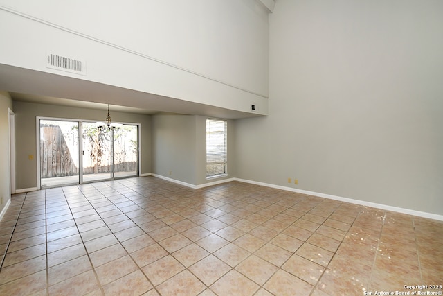 tiled empty room featuring a chandelier and a towering ceiling