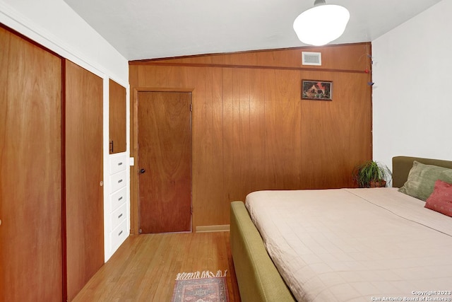 bedroom with a closet, wood walls, light hardwood / wood-style floors, and vaulted ceiling