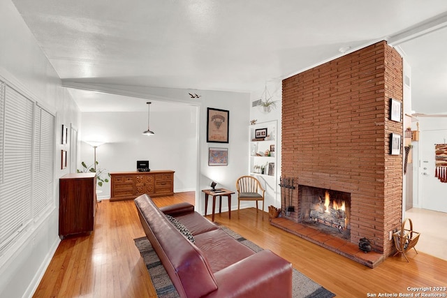 living room featuring brick wall, light wood-type flooring, a fireplace, and lofted ceiling