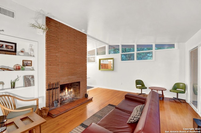 living room featuring brick wall, light hardwood / wood-style floors, vaulted ceiling, and a brick fireplace