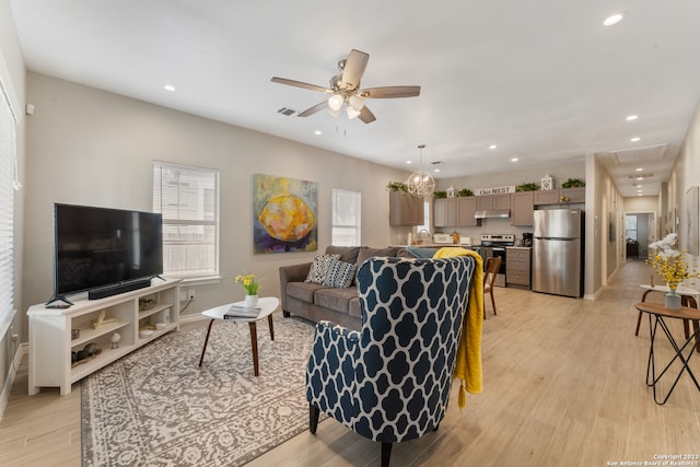 living room featuring sink, light wood-type flooring, and ceiling fan with notable chandelier