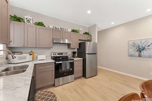 kitchen with gray cabinetry, stainless steel appliances, light hardwood / wood-style flooring, and light stone counters