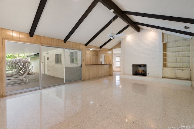 unfurnished living room with beam ceiling, a large fireplace, ceiling fan, wooden walls, and built in shelves