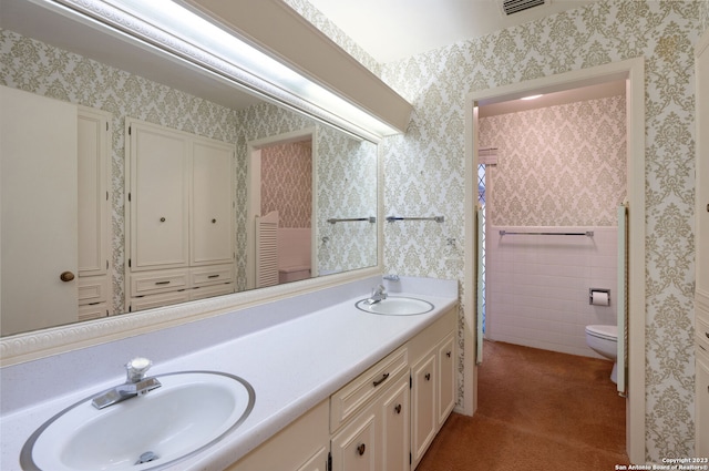 bathroom featuring toilet, dual bowl vanity, and tile walls