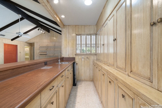 kitchen featuring ceiling fan, light tile floors, sink, wood walls, and vaulted ceiling with beams