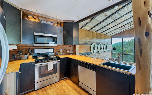 kitchen with wooden walls, sink, light hardwood / wood-style floors, stainless steel appliances, and lofted ceiling