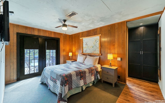 carpeted bedroom featuring wooden walls, ceiling fan, access to outside, and french doors