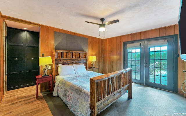 bedroom with wood walls, access to outside, ceiling fan, and french doors