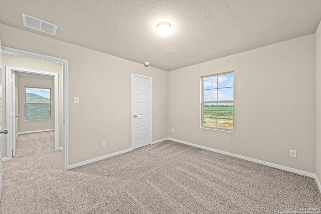 unfurnished bedroom with visible vents, light carpet, a textured ceiling, and baseboards