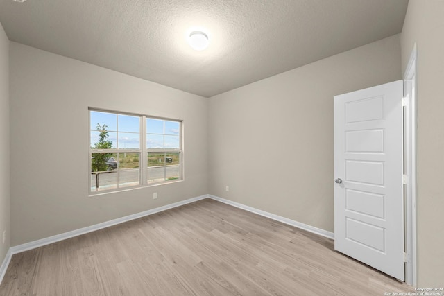 unfurnished room with baseboards, light wood finished floors, and a textured ceiling