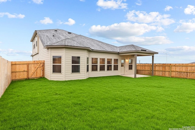 rear view of property featuring a yard, a patio, roof with shingles, and a fenced backyard