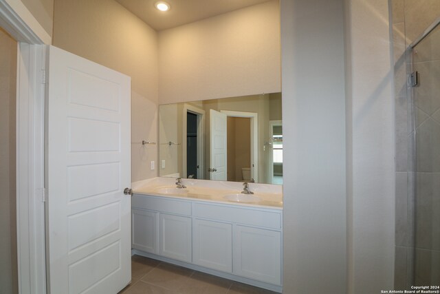 bathroom with tile patterned flooring, toilet, double vanity, tiled shower, and a sink