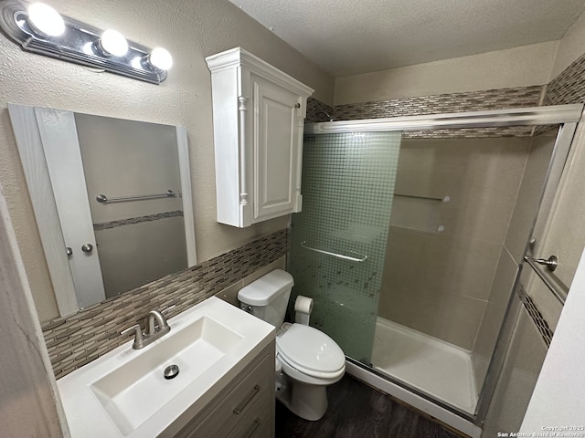 bathroom with toilet, hardwood / wood-style flooring, vanity, tasteful backsplash, and an enclosed shower