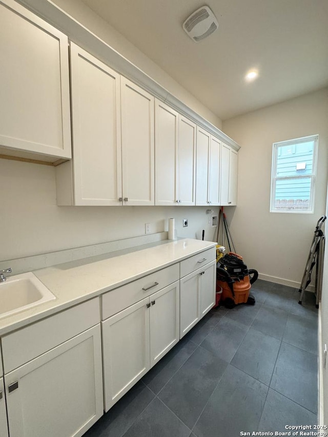 laundry area with hookup for an electric dryer, hookup for a washing machine, cabinets, dark tile patterned flooring, and sink