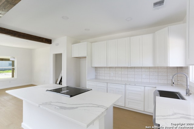 kitchen featuring white cabinets, backsplash, black electric stovetop, and light stone countertops