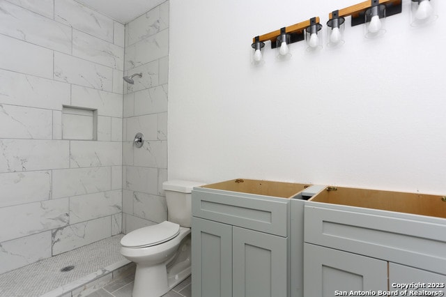 bathroom featuring tile flooring, tiled shower, toilet, and vanity