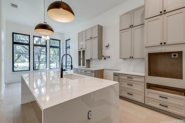 kitchen with light hardwood / wood-style flooring, sink, light stone countertops, and pendant lighting