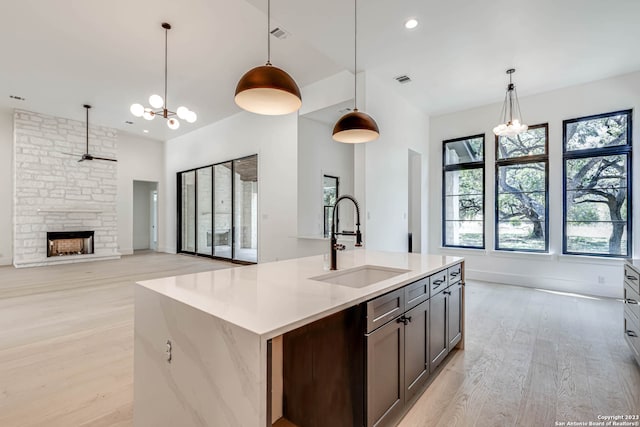 kitchen featuring hanging light fixtures, a kitchen island with sink, a fireplace, sink, and light wood-type flooring