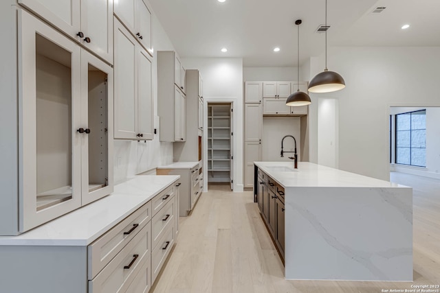 kitchen featuring sink, pendant lighting, light stone counters, a center island with sink, and light wood-type flooring