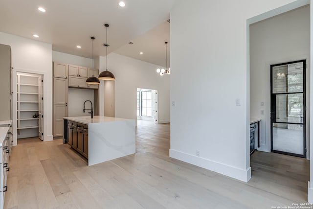 kitchen featuring an island with sink, pendant lighting, sink, light hardwood / wood-style floors, and a notable chandelier