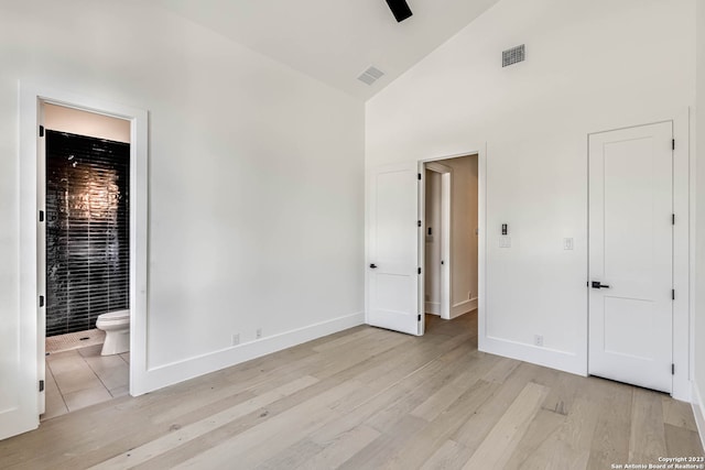 unfurnished bedroom with ceiling fan, ensuite bath, high vaulted ceiling, and light hardwood / wood-style floors