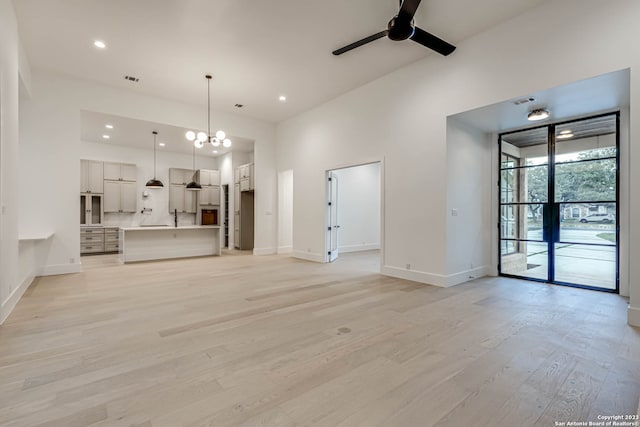 unfurnished living room with light hardwood / wood-style floors, ceiling fan with notable chandelier, and sink