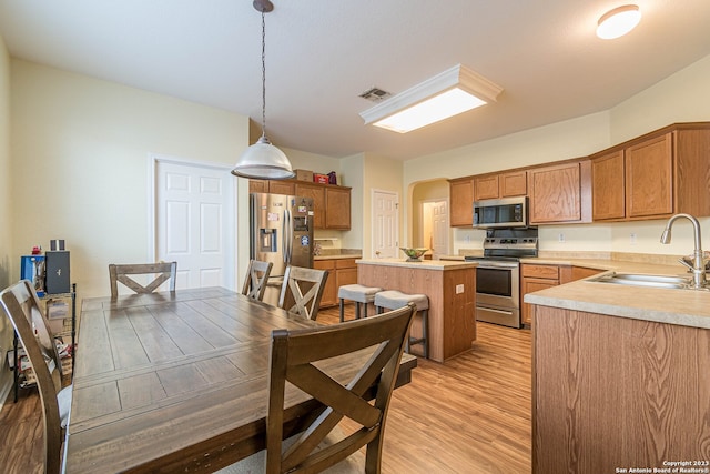 kitchen featuring light hardwood / wood-style floors, a center island, stainless steel appliances, decorative light fixtures, and sink