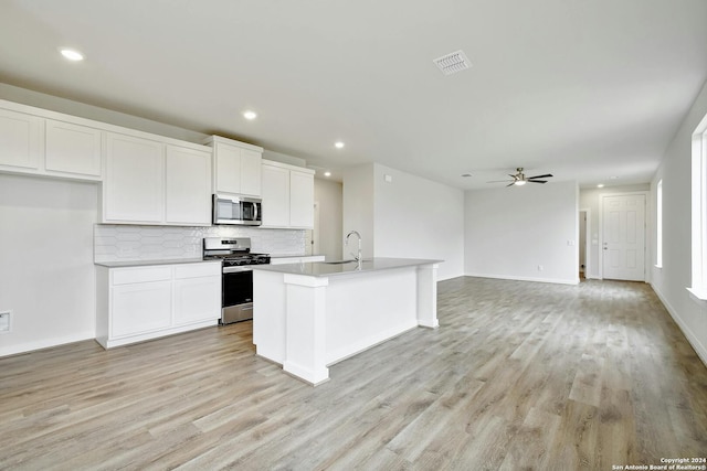 kitchen with stainless steel appliances, light wood-type flooring, a center island with sink, and white cabinets