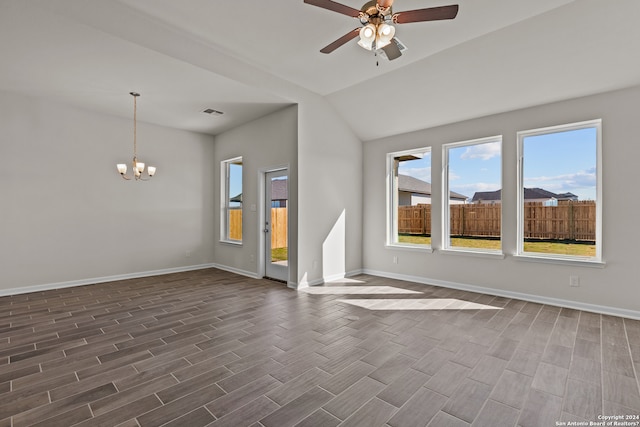 empty room featuring lofted ceiling, ceiling fan with notable chandelier, dark hardwood / wood-style floors, and a wealth of natural light