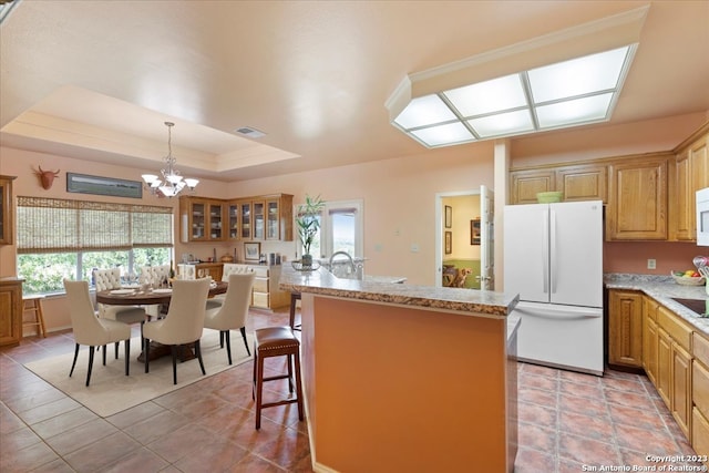 kitchen featuring decorative light fixtures, white appliances, a tray ceiling, a kitchen breakfast bar, and an inviting chandelier