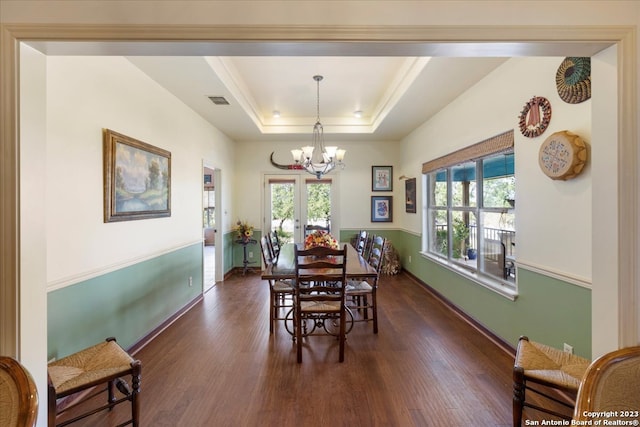 dining area with an inviting chandelier, a wealth of natural light, a tray ceiling, and dark wood-type flooring