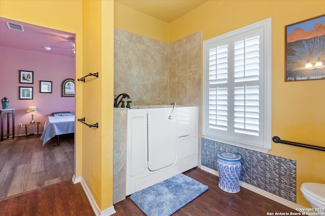 interior space featuring ceiling fan, toilet, a bathing tub, washer / clothes dryer, and hardwood / wood-style flooring