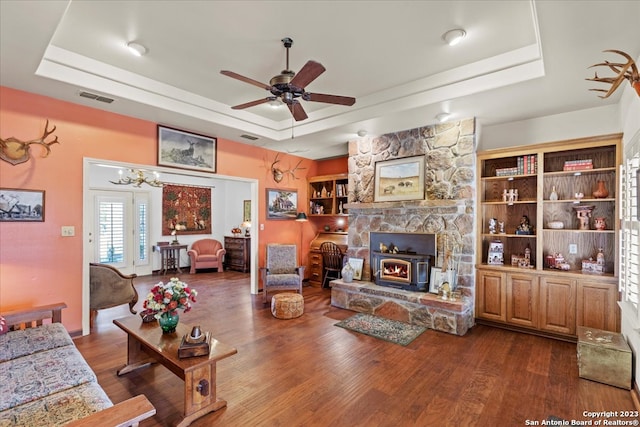 living room featuring a stone fireplace, dark hardwood / wood-style flooring, and a raised ceiling