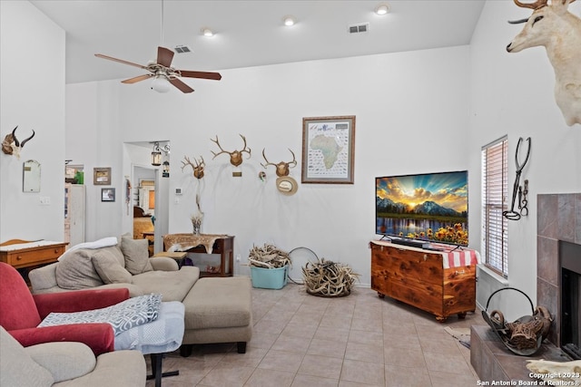 living room with a towering ceiling, ceiling fan, light tile flooring, and a tiled fireplace