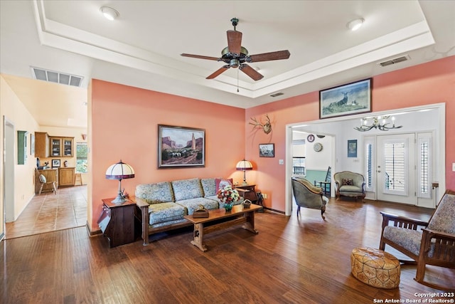 living room featuring ceiling fan with notable chandelier, wood-type flooring, and a tray ceiling