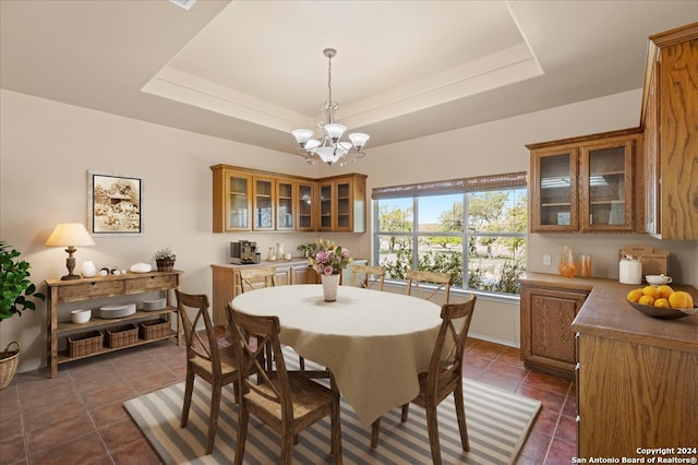 dining space featuring a raised ceiling, a notable chandelier, and dark tile flooring