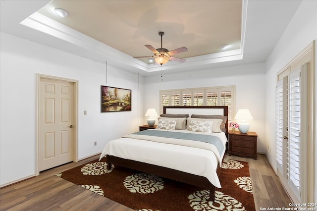 bedroom featuring wood-type flooring, ceiling fan, and a tray ceiling