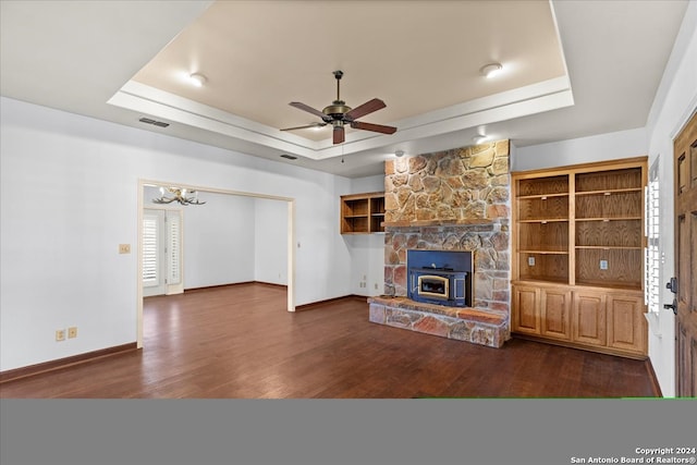 unfurnished living room featuring a stone fireplace, dark wood-type flooring, ceiling fan, and a tray ceiling