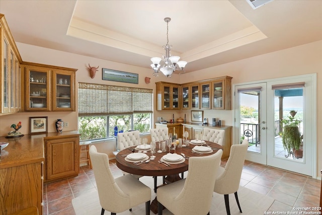 tiled dining space with a healthy amount of sunlight, a raised ceiling, and an inviting chandelier